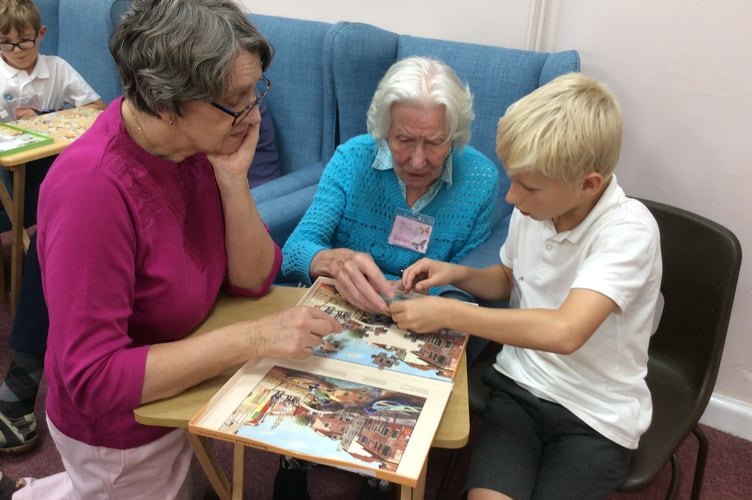 A pupil from St Lawrence CE Primary School in Alton does a jigsaw puzzle with two visitors to The Dementia Café in Alton Community Centre, November 2022.